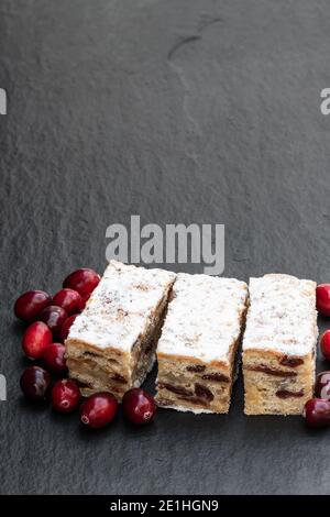 Weihnachtsstollen Scheiben mit Preiselbeere auf schwarzem Stein Hintergrund Stockfoto