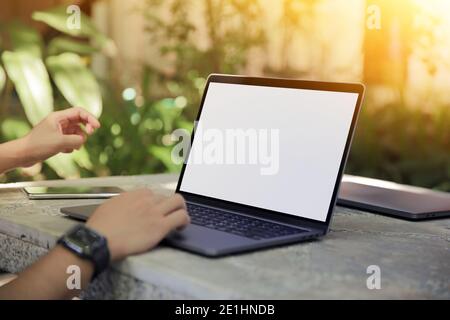 Zugeschnittenes Bild eines jungen Mannes, der in einem Garten an seinem Laptop arbeitet, Rückansicht der Hände eines Geschäftsmanns, der am Büroschreibtisch mit dem Laptop beschäftigt ist und auf Computern tippt Stockfoto