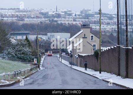 Cork, Irland. Januar 2021. Snow Falls auf Cork City. Der Bus 207 fährt die Ballincollie Road hinunter, gefolgt von einem Fußgänger, der den Wegen trotzt. Die Einwohner von Cork sind heute Morgen nach einem kurzen Schneeschauer in der Stadt und den Vororten aufgewacht, die von einer Schneedecke bedeckt waren. Viele haben sich in Mäntel und Hüte eingewickelt und gingen hinaus, um die frische Luft zu genießen und die schönen Szenen zu sehen. Kredit: Damian Coleman/Alamy Live Nachrichten Stockfoto