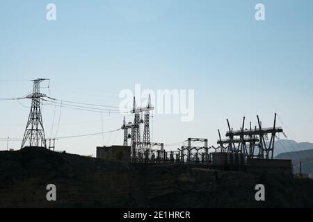 Schwarze Silhouetten von modernen Stromübertragungsleitungen und Türmen an Umspannwerk auf Hügel gegen klaren blauen Himmel am Abend highland Stockfoto