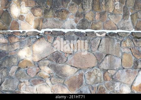 Der Zaun ist aus Naturstein mit Zement mit einem Streifen Schnee verbunden. Textur. Stockfoto