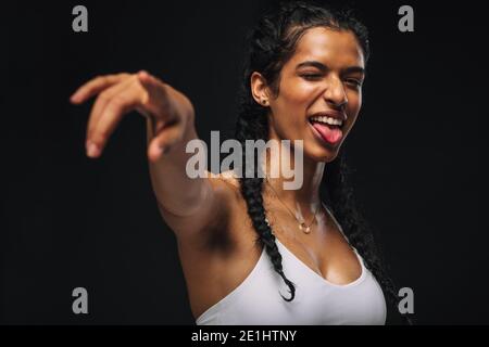 Nahaufnahme Porträt einer Fitness-Frau, die ihre Zunge herausstreckt. Frau in weißen Fitness tragen machen Zeigegeste. Stockfoto