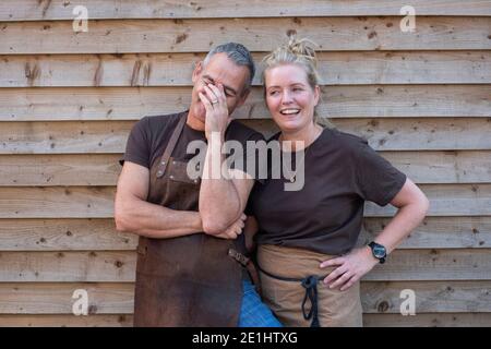 Mann und Frau in Schürzen, Kollegen, die eine Pause von der Arbeit machen, lachen Stockfoto