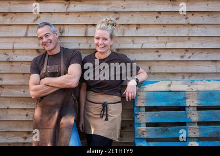 Mann und Frau in Schürzen, Kollegen, die eine Pause von der Arbeit machen, lachen Stockfoto