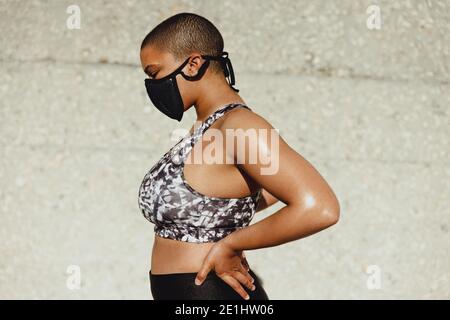 Seitenansicht einer Frau mit muskulösem und gesundem Körper mit Schutzmaske. Fitness-weibliches Modell in Sportbekleidung stehend mit Händen auf der Hüfte. Stockfoto