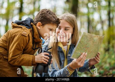 Glückliche Mutter und Sohn wandern im Wald. Junge beobachtet die Natur mit einem Fernglas. Stockfoto