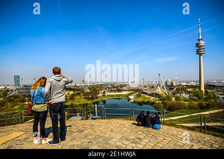 Touristen, die von der Spitze des Hügels auf den Olympiapark und den Turm blicken. München, Deutschland. Foto aufgenommen am 17. April 2019. Stockfoto