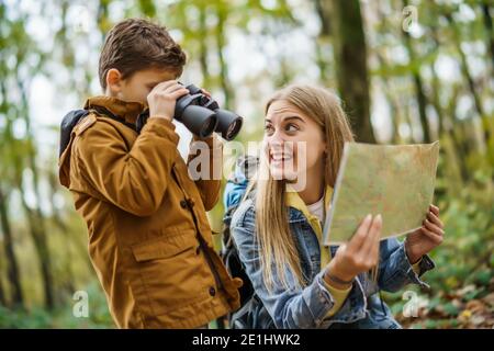 Glückliche Mutter und Sohn wandern im Wald. Junge beobachtet die Natur mit einem Fernglas. Stockfoto