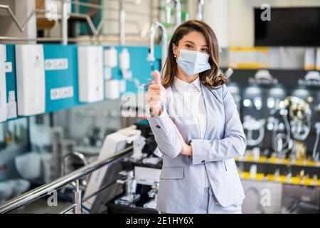 Selbstbewusste Geschäftsfrau, die in ihrem Geschäft steht. Kleinunternehmerin posiert in ihrem Laden, trägt eine schützende Gesichtsmaske. Stockfoto