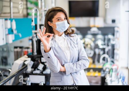Selbstbewusste Geschäftsfrau, die in ihrem Geschäft steht. Kleinunternehmerin posiert in ihrem Laden, trägt eine schützende Gesichtsmaske. Stockfoto