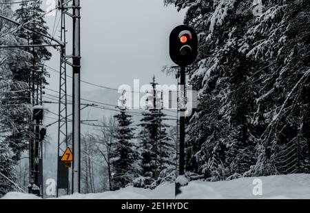 Rote Signalleuchte an einer Bahnlinie mitten im verschneiten Winter. Stockfoto