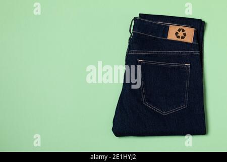 Recycelte blaue Jeans mit einem Kleidungsanhänger. Kreisförmiges Economy-Logo, Zero Waste-Konzept. Wiederverwendung von Materialien und Reduzierung von Abfall in der Mode. Denim horizontal Stockfoto