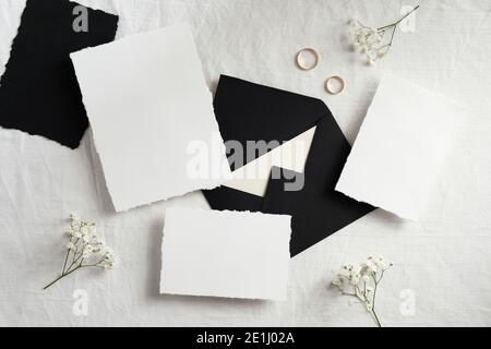 Hochzeit Schreibwaren Mockup Ansicht von oben. Leere Grußkarten, schwarze Umschläge, goldene Ringe, Blumen auf dem Bett. Hochzeitskarten-Design. Stockfoto