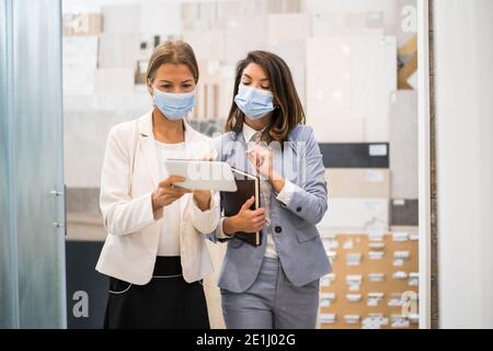Geschäftsfrau, die ein kleines Geschäft im Bad hat. Sie spricht mit einem Kunden, der die Ware wählt. Sie tragen eine schützende Gesichtsmaske. Stockfoto