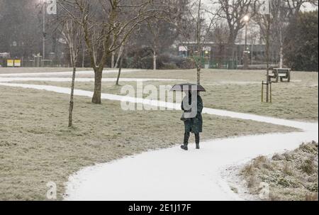 Carrigaline, Cork, Irland. Januar 2021. Schnee beginnt zu fallen, als eine Frau durch den Gemeinschaftspark in Carrigaline, Co. Cork, Irland, geht. - Credit; David Creedon / Alamy Live News Stockfoto