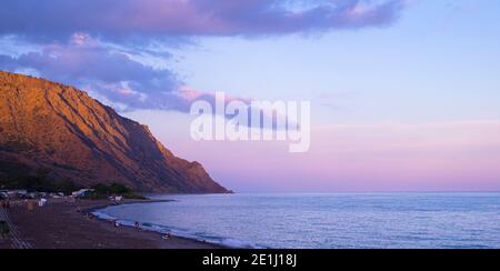 Hintergrund mit Meer Berglandschaft. Sonnenuntergang. Morgendämmerung. Der Himmel und das Meer in lila-rosa Tönen. Schwarzer Sand. Sonnenbeschienenen Bergen. . Camping am Meer. Stockfoto