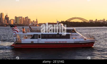 Ein Ausflugsboot auf dem Sydney Harbour, Australien, bei Sonnenuntergang, mit dem Sydney Opera House und der Harbour Bridge im Hintergrund Stockfoto