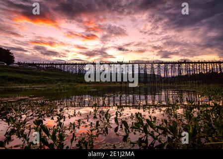 Die Landschaft der Spiegelung der Silhouette hölzerne Mon Brücke in der Sonnenuntergangszeit in Sangkhlaburi, Kanchanaburi, Thailand. Stockfoto