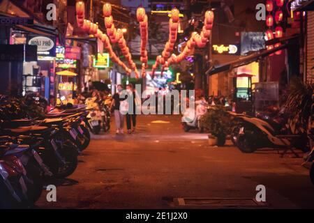 Zwei unverkennbare Frauen in Masken auf der Nachtstraße. Verschwommene asiatische Gasse mit chinesischen Laternen und Neonschildern. Vietnam, Ho Chi Minh: 2020-12 Stockfoto