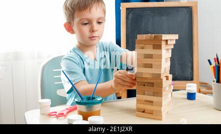 Intelligenter Junge, der Holzblöcke aus dem hohen Turm aus Ziegelsteinen zieht. Konzept von intelligenten Kindern und häuslicher Bildung während des Lockdown und der Selbstisolation. Stockfoto