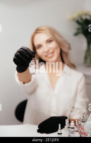 Flasche mit rotem Pigment für Lippen Tattoo in den Händen von verschwommenen weiblichen permanenten Make-up Master. Flaschen mit Tinten auf dem Tisch im Salon ohne Etikett. Auswahl Stockfoto