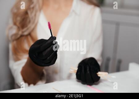 Rosa Bürste für dauerhafte Make-up in den Händen der weiblichen Meister in schwarzen Handschuhen, selektive Fokus. Kosmetikerin Werkzeug für die Herstellung Augenbrauen Make-up. Gesichtspflege und Stockfoto