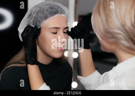 Permanent Master zeichnet Linien mit Faden auf dem Gesicht des Kunden, macht eine Skizze der Augenbrauen. Augenbraue dauerhafte Make-up Verfahren, Microblading. Schönheit Konz Stockfoto