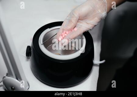 Nahaufnahme der weiblichen Hand in einem Handschuh mit rosa Wachs vor dem Schmelzen. Enthaarungskonzept, Wachsen, glatte Haut ohne Haare. Schönheitssalon Gerät für ihn Stockfoto