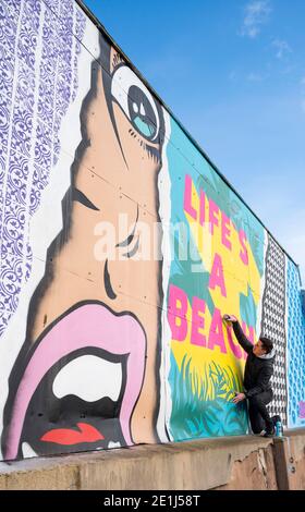 Lancing West Sussex UK 7. Januar 2021 - der Street-Artist Luke Henley, bekannt als Wooze, setzt seinen letzten Schliff an seinem neuesten Stück "Life's A Beach" an der Lancing Seafront in der Nähe von Worthing in West Sussex . Der Künstler erhielt die Erlaubnis, das Kunstwerk auf einer Wand hinter einer lokalen Garage mit Blick auf Lancing Green zu schaffen und er hofft, dass es die Gegend für Wanderer und Besucher erhellt : Credit Simon Dack / Alamy Live News Stockfoto