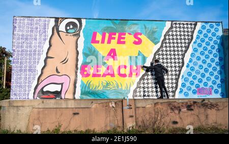 Lancing West Sussex UK 7. Januar 2021 - der Street-Artist Luke Henley, bekannt als Wooze, setzt seinen letzten Schliff an seinem neuesten Stück "Life's A Beach" an der Lancing Seafront in der Nähe von Worthing in West Sussex . Der Künstler erhielt die Erlaubnis, das Kunstwerk auf einer Wand hinter einer lokalen Garage mit Blick auf Lancing Green zu schaffen und er hofft, dass es die Gegend für Wanderer und Besucher erhellt : Credit Simon Dack / Alamy Live News Stockfoto