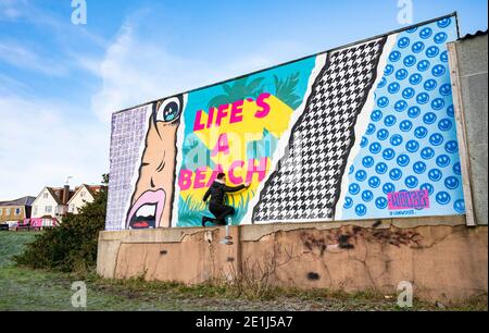 Lancing West Sussex UK 7. Januar 2021 - der Street-Artist Luke Henley, bekannt als Wooze, setzt seinen letzten Schliff an seinem neuesten Stück "Life's A Beach" an der Lancing Seafront in der Nähe von Worthing in West Sussex . Der Künstler erhielt die Erlaubnis, das Kunstwerk auf einer Wand hinter einer lokalen Garage mit Blick auf Lancing Green zu schaffen und er hofft, dass es die Gegend für Wanderer und Besucher erhellt : Credit Simon Dack / Alamy Live News Stockfoto