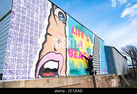 Lancing West Sussex UK 7. Januar 2021 - der Street-Artist Luke Henley, bekannt als Wooze, setzt seinen letzten Schliff an seinem neuesten Stück "Life's A Beach" an der Lancing Seafront in der Nähe von Worthing in West Sussex . Der Künstler erhielt die Erlaubnis, das Kunstwerk auf einer Wand hinter einer lokalen Garage mit Blick auf Lancing Green zu schaffen und er hofft, dass es die Gegend für Wanderer und Besucher erhellt : Credit Simon Dack / Alamy Live News Stockfoto
