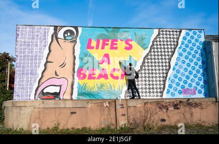 Lancing West Sussex UK 7. Januar 2021 - der Street-Artist Luke Henley, bekannt als Wooze, setzt seinen letzten Schliff an seinem neuesten Stück "Life's A Beach" an der Lancing Seafront in der Nähe von Worthing in West Sussex . Der Künstler erhielt die Erlaubnis, das Kunstwerk auf einer Wand hinter einer lokalen Garage mit Blick auf Lancing Green zu schaffen und er hofft, dass es die Gegend für Wanderer und Besucher erhellt : Credit Simon Dack / Alamy Live News Stockfoto