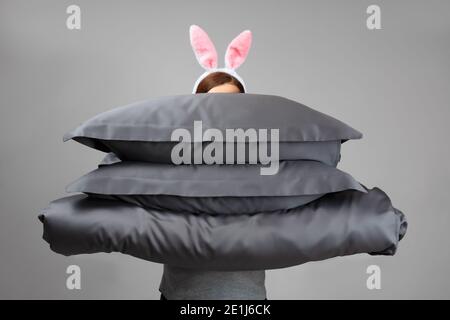 Eine Frau in Osterhasen-Ohren hält eine warme Bettdecke und graue Federkissen. Bettwäsche zum Schlafen. Stockfoto