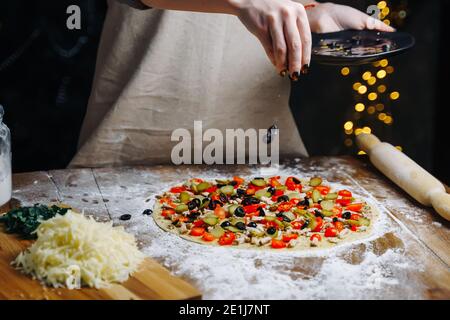 Hausgemachte Pizza Kochen. Frau Hand kochen Gießen Oliven Scheiben auf Teig. Konzept für die Zubereitung von Lebensmitteln unter Quarantäne aufgrund von Epidemien. Stockfoto