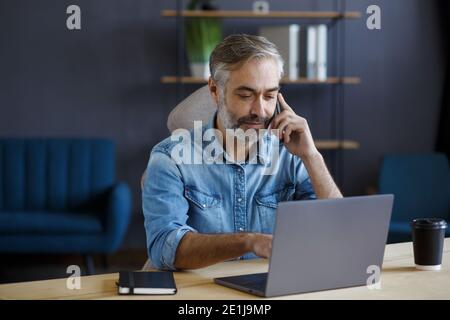 Leitender grauhaariger Geschäftsmann, der im Büro telefoniert. Gespräch mit Geschäftspartnern. Geschäftsporträt des hübschen reifen Mannes sitzend Stockfoto
