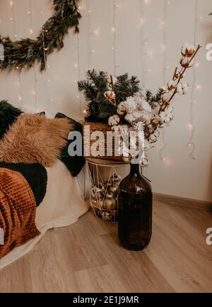 Helles Schlafzimmer in einem minimalistischen Stil mit einem Weihnachtsbaum mit Girlanden und Trockenpflanzen in einer Vase dekoriert. Weihnachtsmorgen. Das Interieur des neuen Jahres. V Stockfoto