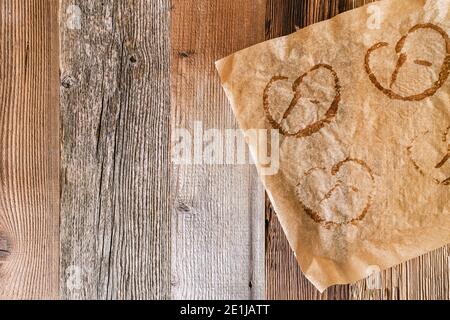 Gebrautes Backpapier mit Abdrücken von gebackenen Brezeln auf rustikalem Holzhintergrund. Brezeln sind typisch deutsche Küche in Bayern und auf dem Oktoberfest. Stockfoto