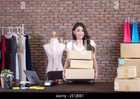 Schöne asiatische Frau, die zwischen mehreren Boxen und Pakete überprüfen, im Büro des Hauses arbeiten. Konzept für Home Base Business und Startup-Besitzer Stockfoto
