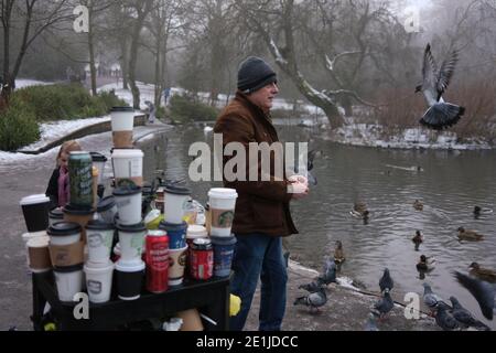 Glasgow, Großbritannien, 7. Januar 2021. Mann, der Tauben füttert, neben Abfalleimer, die mit gebrauchten Einweg-Kaffeetassen überfüllt sind, und Abfall nach einem arbeitsreichen Wochenende im Park, das bei schönem Winterwetter zusammenfällt, im Queen's Park im Süden der Stadt. Foto: Jeremy Sutton-Hibbert/Alamy Live News Stockfoto