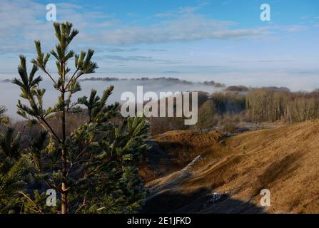 Atemberaubende Winteransicht von Painswick Beacon in den Cotswolds suchen Über das nebelgefüllte Tal zum Snow Capped Hügel am Horizont Stockfoto