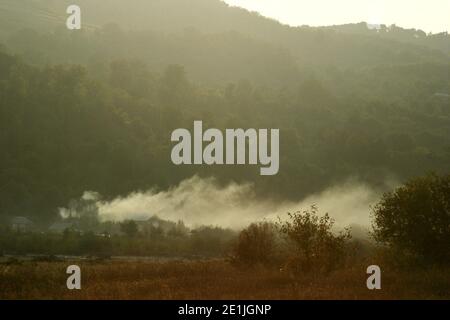 Landschaft auf dem Land Rumäniens. Rauch kommt aus einem Feld neben den Häusern. Stockfoto