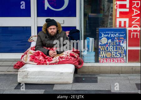 Slough, Berkshire, Großbritannien. Januar 2021. Ein Obdachloser sitzt auf einer Matratze im Foyer von WH Smith in der Slough High Street. Slough war heute am zweiten Tag der neuen Covid-19 Nationalsperre viel ruhiger als sonst. Die Zahl der positiven Covid-19-Fälle in Slough ist außer Kontrolle geraten. Für die sieben Tage bis zum 2. Januar 2021 waren die Zahlen pro 100,000 für Slough 1064.6 gegenüber 722.2. Die durchschnittliche Zahl in ganz England ist nur 606.9 für den gleichen Zeitraum. Quelle: Maureen McLean/Alamy Live News Stockfoto