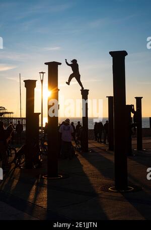 Brighton UK 7. Januar 2021 - Free Runners springen von Säule zu Säule der Golden Spiral Kunstinstallation in der Nähe des West Pier an der Küste von Brighton, während die Sonne nach einem schönen Tag an der Südküste untergeht : Credit Simon Dack / Alamy Live News Stockfoto