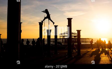 Brighton UK 7. Januar 2021 - Free Runners springen von Säule zu Säule der Golden Spiral Kunstinstallation in der Nähe des West Pier an der Küste von Brighton, während die Sonne nach einem schönen Tag an der Südküste untergeht : Credit Simon Dack / Alamy Live News Stockfoto