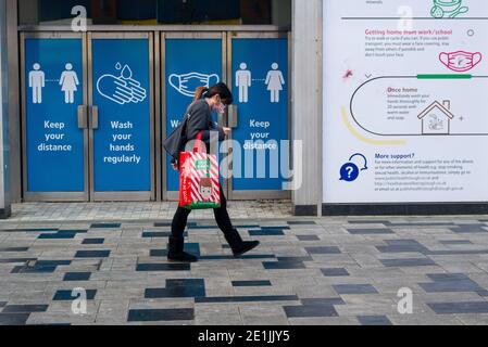 Slough, Berkshire, Großbritannien. Januar 2021. Ein Shopper geht an den Schildern Covid-19 in der Slough High Street vorbei. Slough war heute am zweiten Tag der neuen Covid-19 Nationalsperre viel ruhiger als sonst. Die Zahl der positiven Covid-19-Fälle in Slough ist außer Kontrolle geraten. Für die sieben Tage bis zum 2. Januar 2021 waren die Zahlen pro 100,000 für Slough 1064.6 gegenüber 722.2. Die durchschnittliche Zahl in ganz England ist nur 606.9 für den gleichen Zeitraum. Quelle: Maureen McLean/Alamy Live News Stockfoto