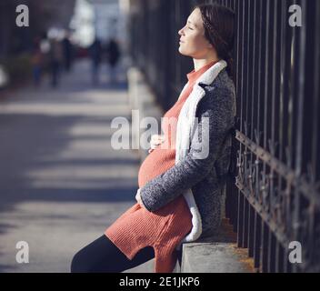 Glücklich schwangere junge Frau hält ihren Bauch im Freien in der Stadt Stockfoto