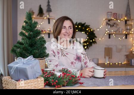 Frau, die an einem Tisch sitzt und heiße Schokolade trinkt weihnachtlich dekoriertes Zimmer Stockfoto