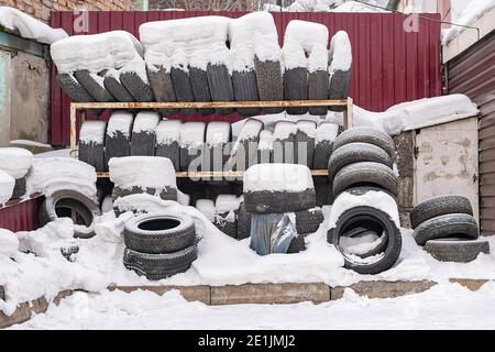 Eine Menge, ein Haufen abgenutzter, gebrauchter Autoreifen, Reifen Räder liegen auf einem Rack im Freien im Winter im Schnee Stockfoto