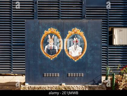 Graffiti Street Art farbenfrohe Gemälde auf Metall Power Box mit Vintage gerahmten Porträts von gekleideten humanisierten Kaninchen und Hühnern auf Blau Stockfoto